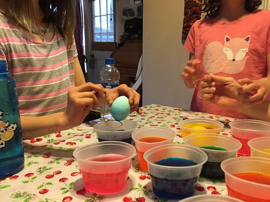 two young girls dyeing Easter eggs at a table