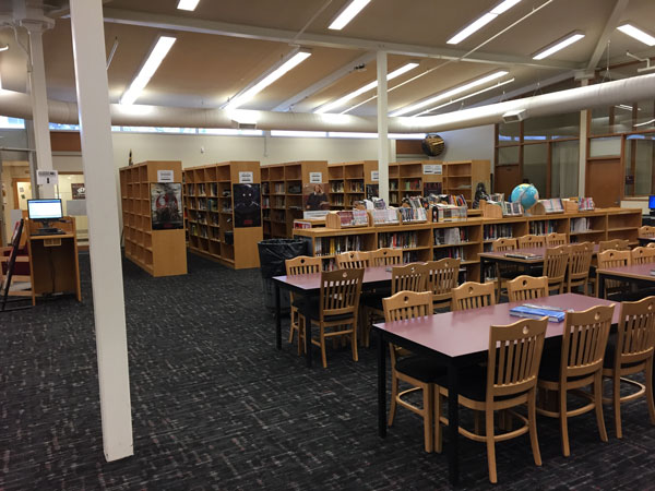 High school library with partially filled shelves of books, and tables and chairs in the foreground