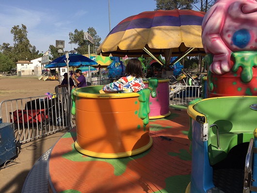 girl in hooded top sitting in spinning carnival ride