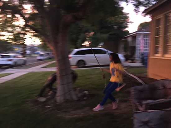 blurry photo of girl with brown hair, yellow shirt, and blue leggings on swing, at sunset