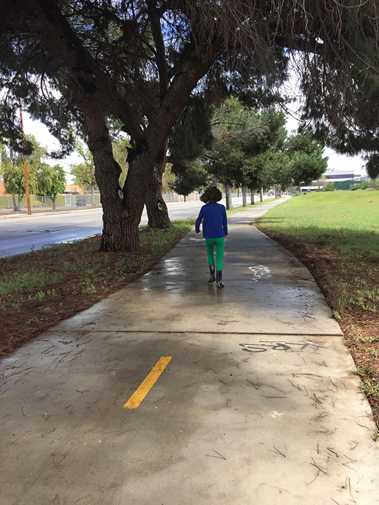 girl with brown hair wearing dark blue shirt, green leggings, and rain boots walking away from camera