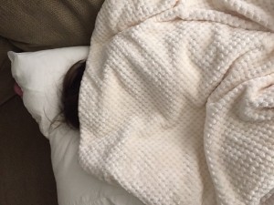 crown of person's head with brown hair peeking up above an off-white waffle-weave blanket