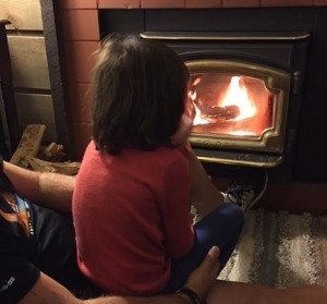 Little girl sitting in front of a small fireplace with a glass front