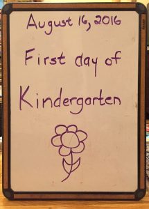 white board with date and "first day of kindergarten" written on it, and a drawing of a flower