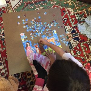 small girl working on 250-piece puzzle with an image of a girl, rabbits, fox, tree, flowers, and deer